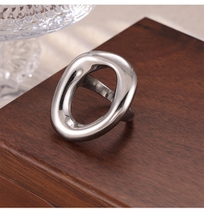 Macro detail of a silver irregular hollow oval ring with a polished mirror finish on wood