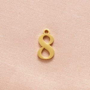 Close-up of golden number 8 pendant in stainless steel on pink fabric background