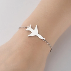 Detailed view of a minimalist silver airplane pendant on a stainless steel chain bracelet