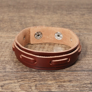Detailed view of brown multi-layer leather bracelet with metal snap buttons on wood