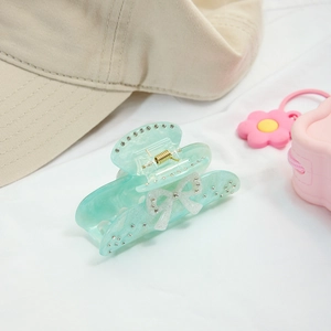 Detailed view of mint green acetate hair claw with white bow and sparkling rhinestones