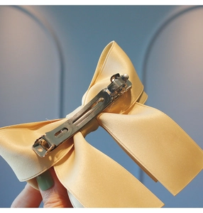 Detailed close-up of cream satin bow hair clip with a sturdy silver metal spring fastener