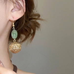Gros plan de boucles d'oreilles sphériques dorées avec perles de résine verte sur un mannequin