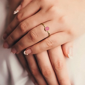 Detail of a gold pavé ring with pink gemstones on fingers against a soft white fabric