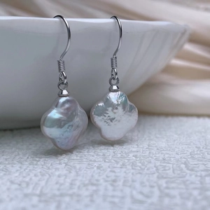 Macro detail of baroque clover-shaped pearl earrings with silver hooks on porcelain