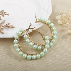 Detail of gold circle earrings featuring hand-wrapped mint green pearls on a ceramic plate
