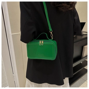 Detail of green crossbody bag with dual gold zippers and adjustable shoulder strap