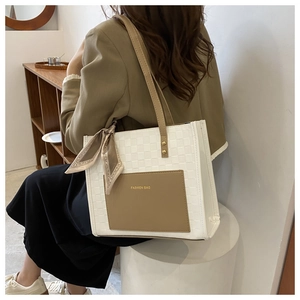 Detail of checkered cream and brown tote bag with decorative silk scarf on model