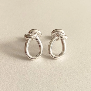 Macro shot of minimalist polished silver knot stud earrings on a beige surface