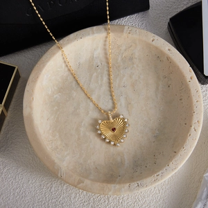 Close-up of heart-shaped gold necklace with red and white stones on marble