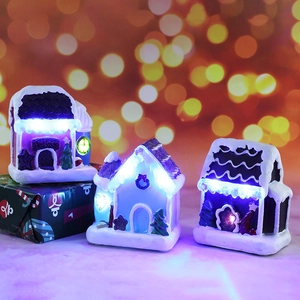 Three LED glowing resin Christmas house ornaments with snow scenery in a festive bokeh scene