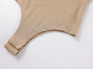 Close-up of metal snap button closure and knit fabric detail on khaki cotton bodysuit