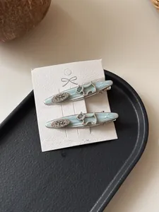 Detail of light blue surfboard hair clips with silver dog motif on display tray