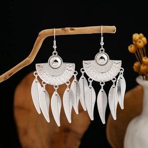 Detailed shot of ethnic silver fan earrings with leaf tassels hanging on a wood branch