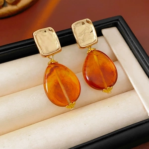Macro detail of amber teardrop pendant earring with gold hammered texture on a jewelry box cushion