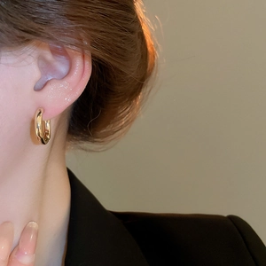 Close-up of a minimalist round gold hoop earring with a high-shine polished finish