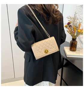 Detailed view of beige quilted flap bag with gold round lock and chain strap