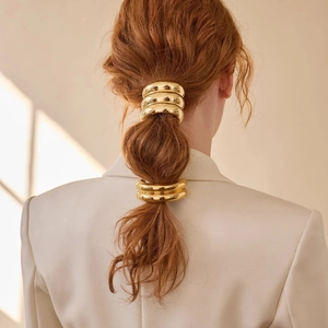 Detailed view of layered polished gold metal hair rings on a ponytail hairstyle