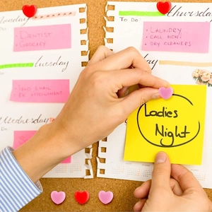 Close-up of red and pink heart-shaped push pins on a cork board with notes