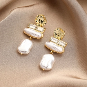 Detailed macro of baroque pearl drop earrings with crystals on champagne silk background