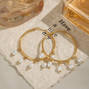 Elegant gold hoop earrings with white pearl tassels on a textured decorative paper background