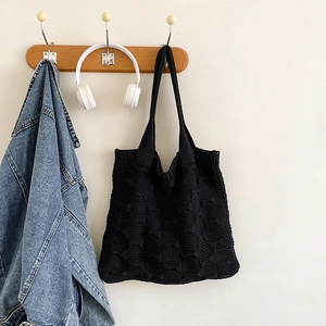 Detail of a black knit tote bag with 3D diamond pattern hanging on a wooden wall hook