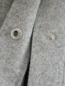 Detailed macro view of silver snap button on grey wool blend fabric jacket