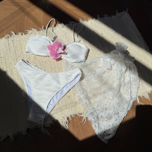 Close-up of white three-piece bikini with floral decor and lace sarong on rug