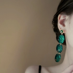 Detail of vintage emerald geometric drop earrings with gold-tone accents on model