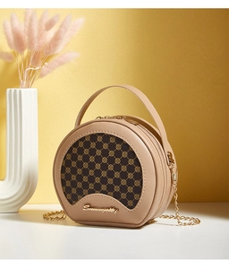 Détail du sac bandoulière rond beige avec motifs de trèfle brun et chaîne dorée chic