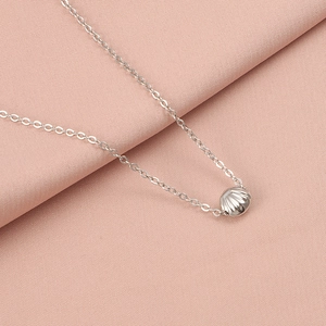 Detailed view of silver shell pendant on stainless steel chain over pink fabric