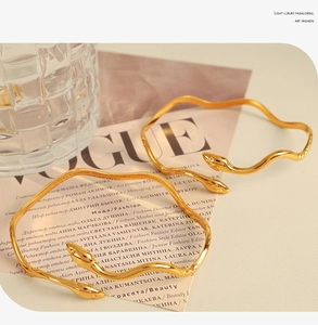 Detailed view of two gold serpent bangles with polished finish on a magazine background