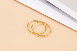 Detail of mirror-polished gold hoop earrings with seamless hinge on a warm beige background