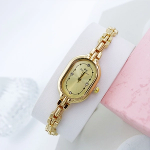 Montre-bracelet dorée ovale pour femme avec strass présentée sur un coussin d'affichage
