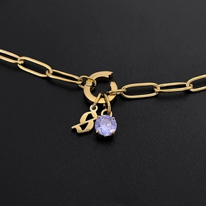 Close-up of gold paperclip chain necklace with gothic letter S and purple zircon pendant.