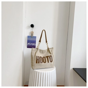 Detail of the cream canvas tote bag featuring brown leather HOOTO letters and chain strap