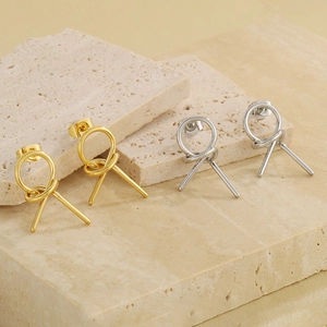 Detail of minimalist knotted geometric stud earrings in gold and silver finishes