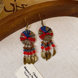 Detail of bohemian earrings with red and blue thread, crystal beads, and metal leaf charms