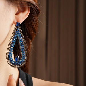 Macro side view of elegant teardrop earrings with blue crystals on a female model
