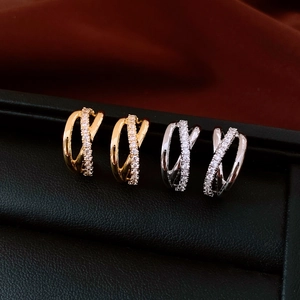 Crossed gold and silver earrings with zircon stones displayed in a jewelry box