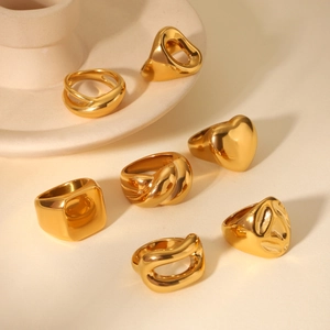 Close-up of assorted gold chunky rings including heart and croissant shapes on ceramic