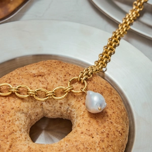 Baroque pearl necklace with gold chain links elegantly displayed on a creative bagel setting