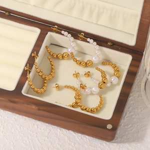 C-shaped gold bead and pearl stainless steel hoop earrings in a wooden jewelry box