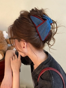 Detailed close-up of a denim bow hair claw clip with burgundy trim on a model's hair