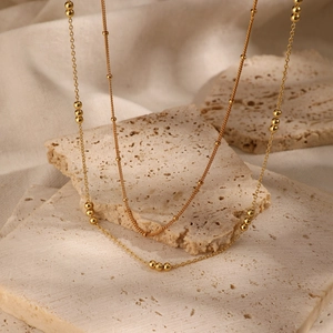 Minimalist double layer gold beaded necklace draped over natural beige stone textures