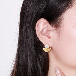 Close-up of golden semicircular earrings with white circular accents on a female model