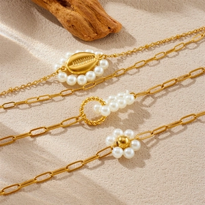 Bracciale retrò placcato oro con perle, conchiglie e dettagli a nodo su fondo sabbia calda