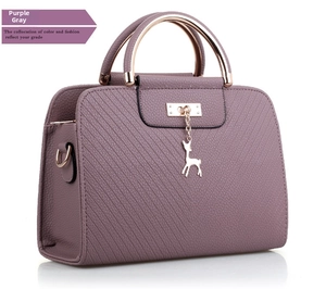 Detail of purple embossed leather handbag featuring metal ring handle and deer charm pendant