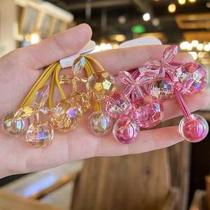 Detailed shot of translucent cherry charms on colorful elastic hair ties held in hand