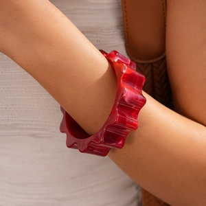 Close-up of a thick red translucent acrylic bracelet with scalloped wave edges on wrist